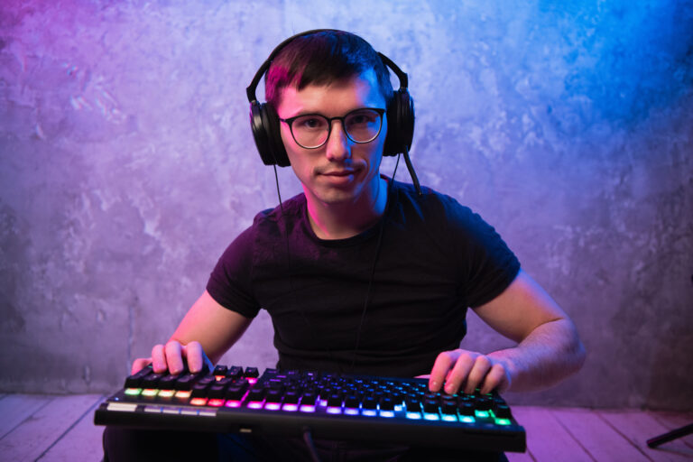 Portrait of the young handsome pro gamer sitting on the floor with keyboard in neon colored room